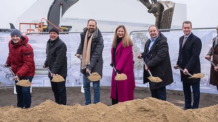 Acht Personen mit Schaufeln in den Händen vor einem Erdhaufen