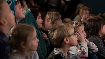 Mehrere Kinder schauen gespannt auf eine Bühne, die sich außerhalb des Bildes befindet