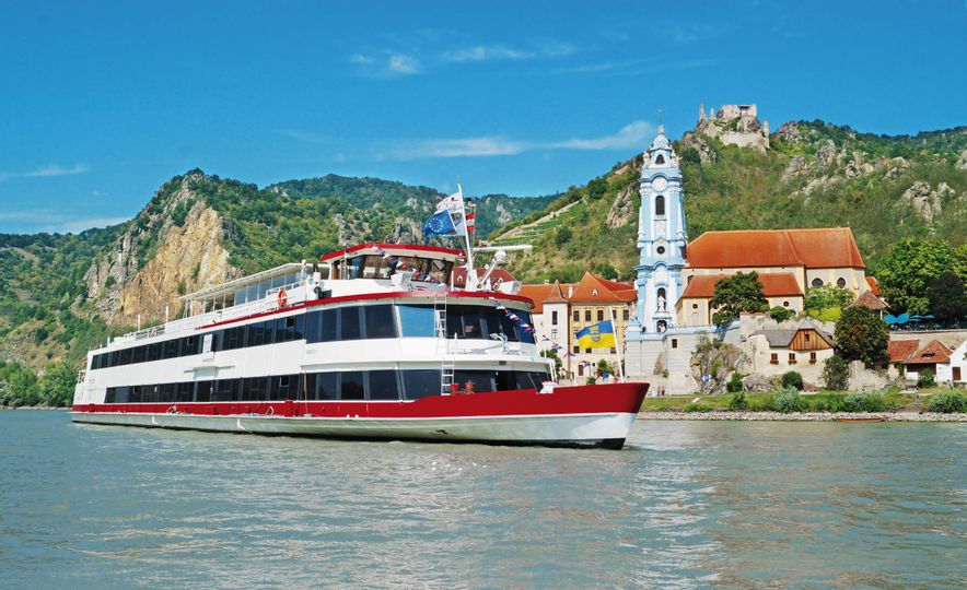 Ein Schiff der DDSG Blue Danube Schifffahrt GmbH fährt auf der Donau, im Hintergrund ist Dürnstein zu sehen.